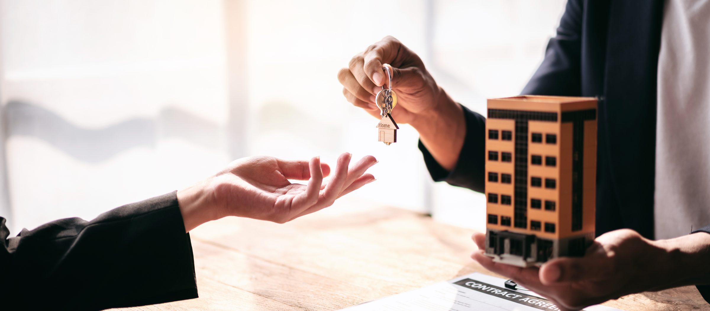 An adviser handing over house keys beside a model building